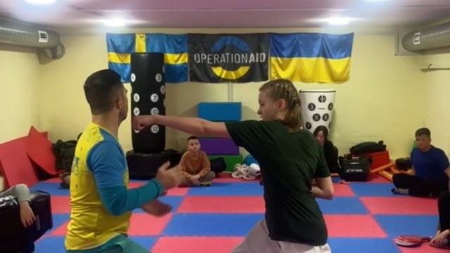 Barn tränar jiu-jitsu i ActiveKids Cherson, framför svenska och ukrainska flaggan tillsammans med OperationAids logotyp.